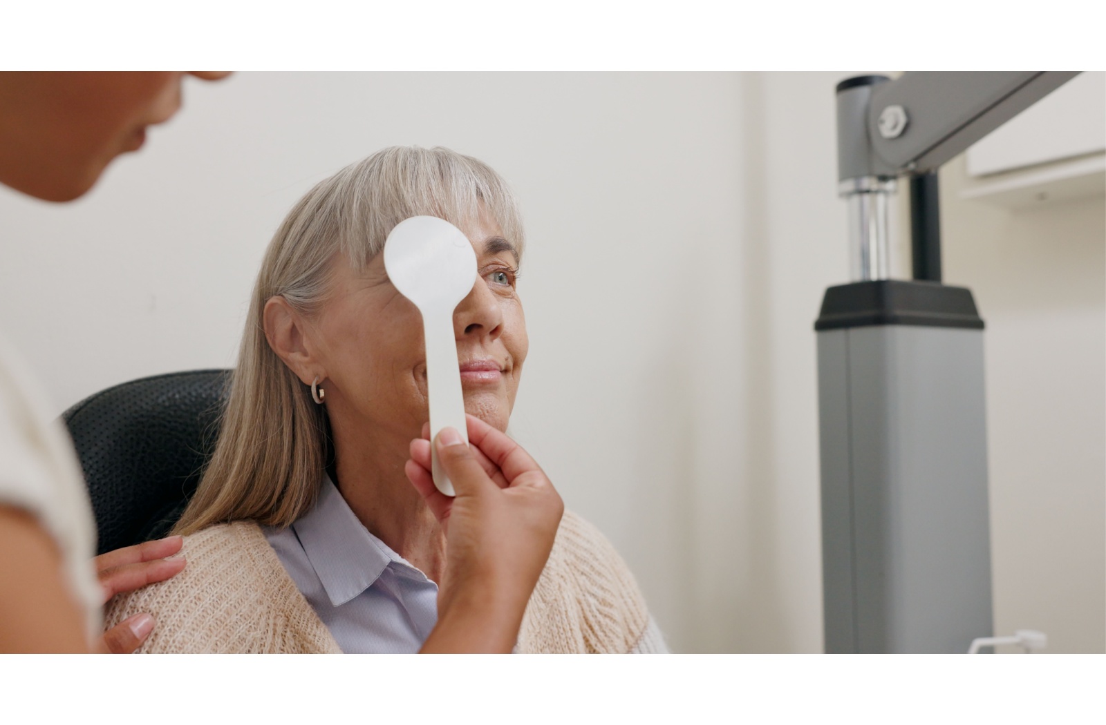 An older woman covering one eye during a vision test at an optometry clinic, assisted by an optometrist during a routine eye exam.