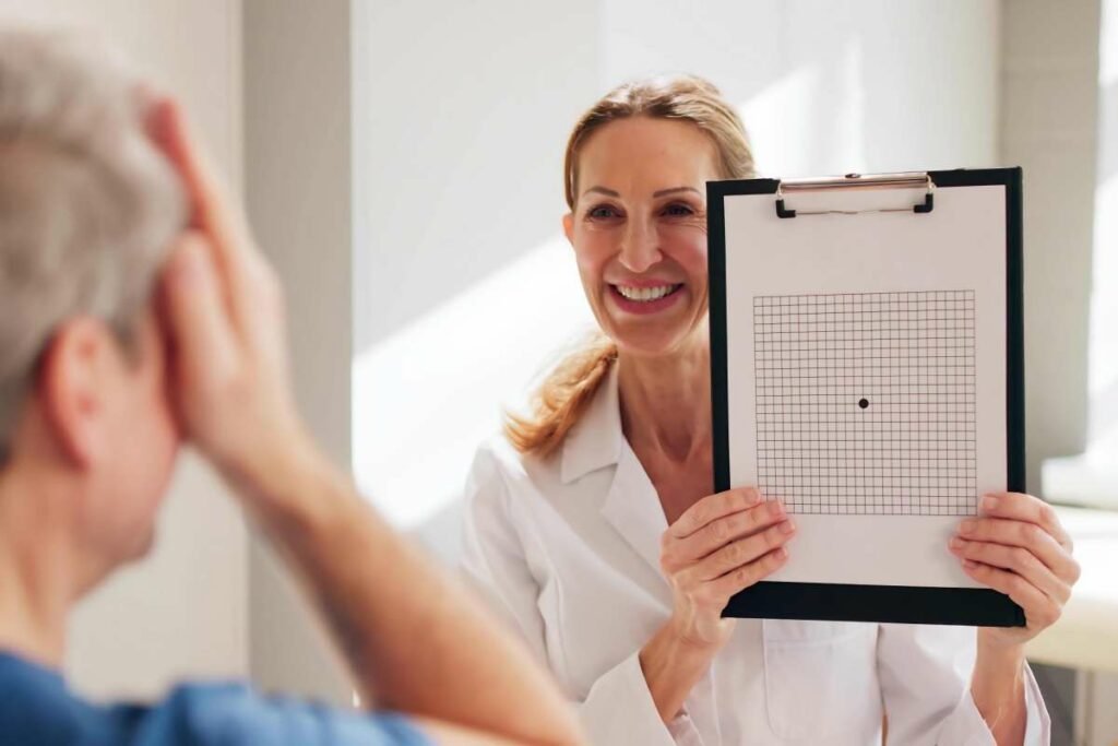 Optometrist smiling while holding an Amsler grid during a macular health screening, with a patient covering one eye.
